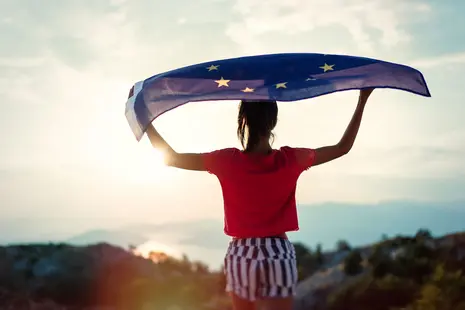 Child girl teenager young person is waving European Union flag on top of mountain at sky background. Sunset time